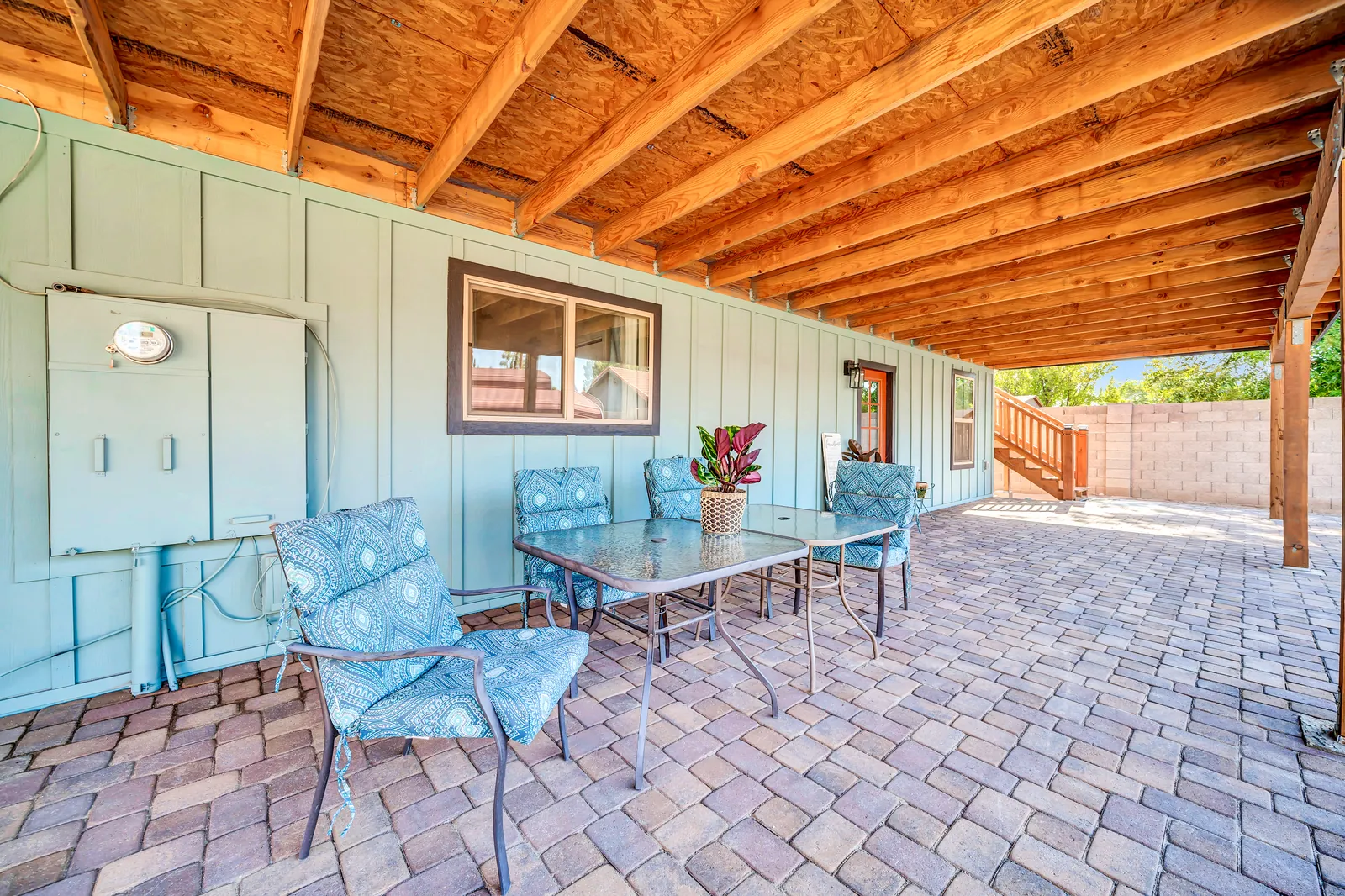Patio chairs and a glass table along the green barn wall, under the pergola.