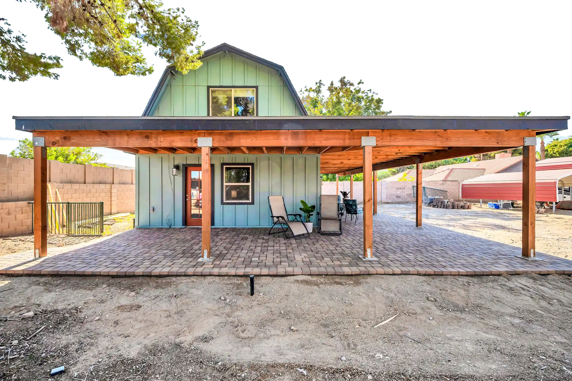 The green barn at Oasis on Orangewood, with its timber pergola and brick patio, under a clear sky.