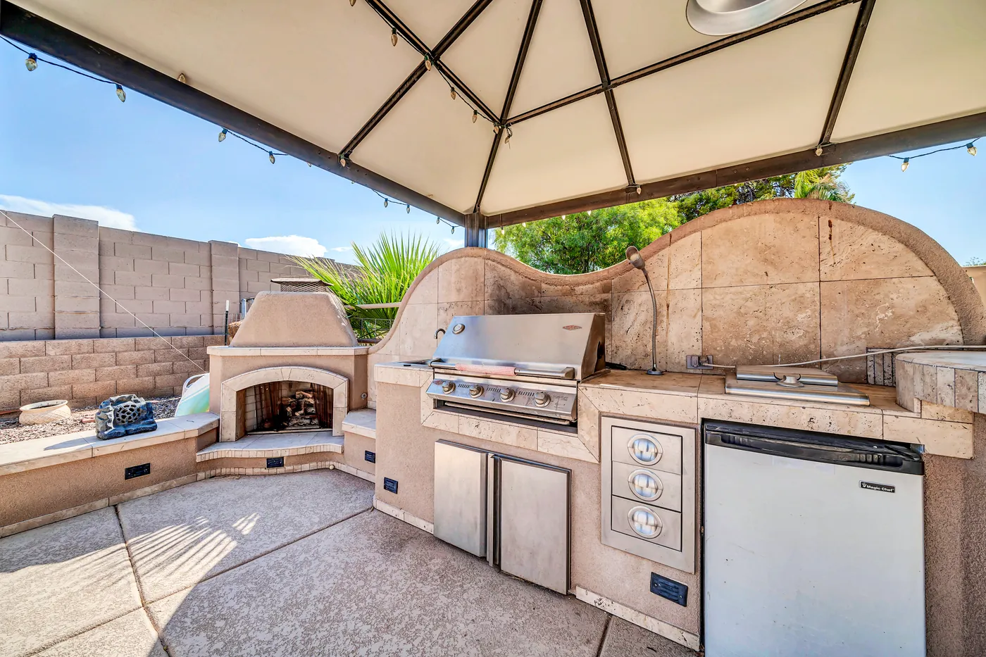 The outdoor kitchen and fireplace under a canopy strung with lights.