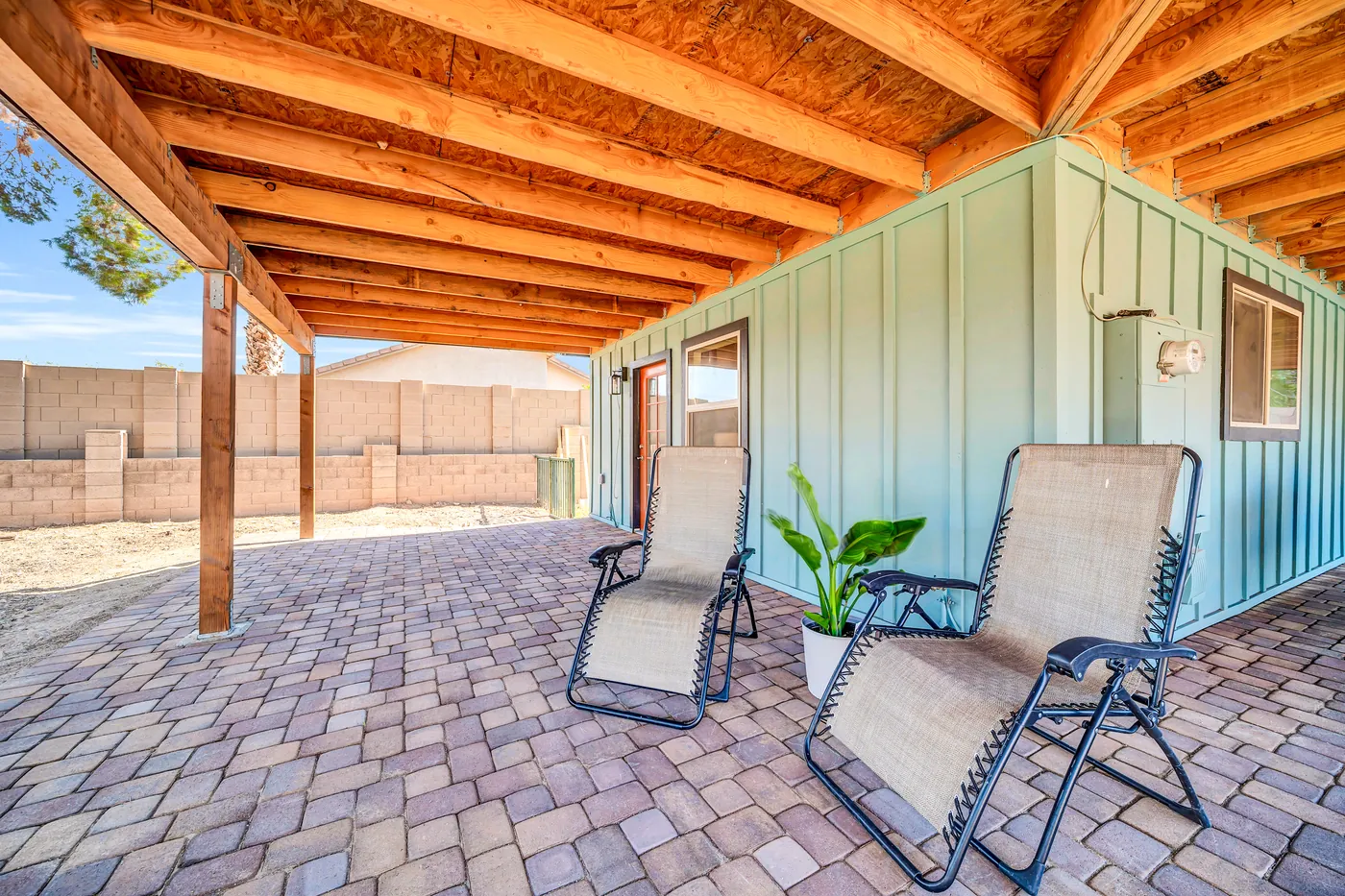 Two lounge chairs side by side on the brick patio under the barn's timber pergola.