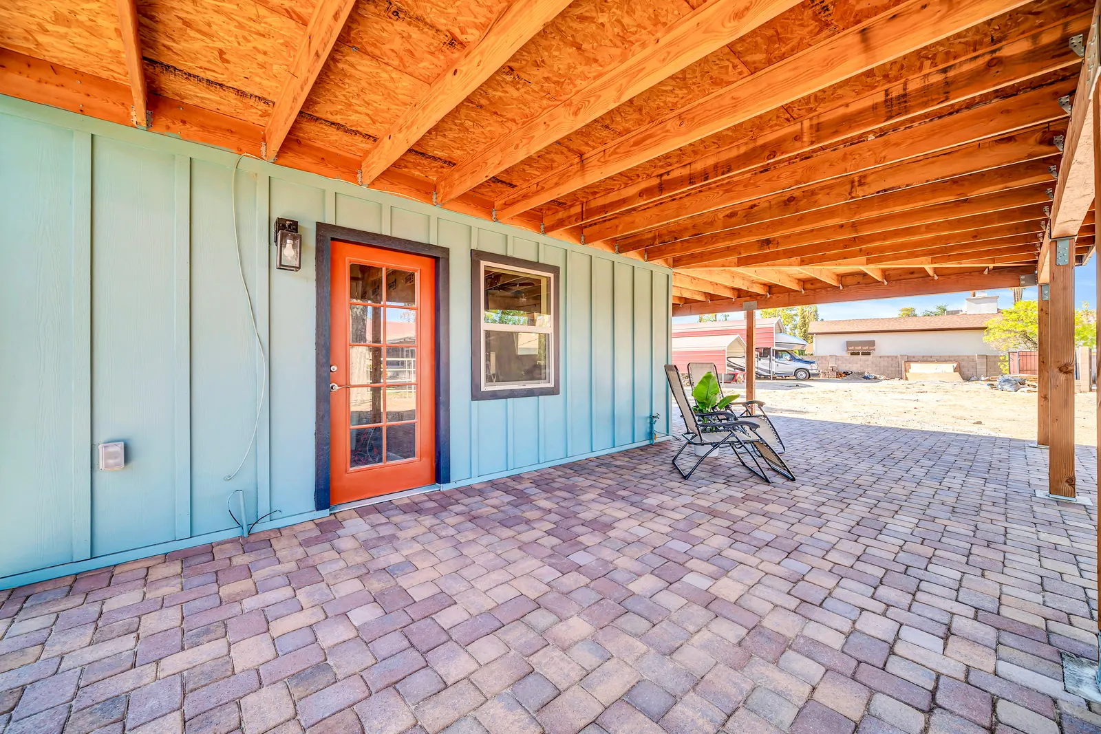 A bright orange glass-paned door in the green barn wall, opening onto the paved patio.