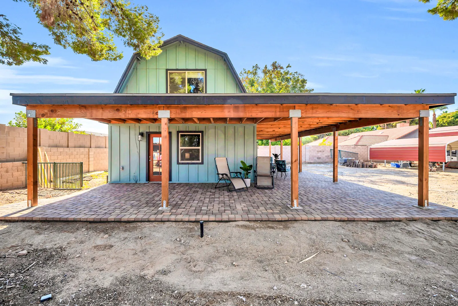 The converted barn seen from its paved patio under a timber-framed roof, with the green board-and-batten apartments behind.