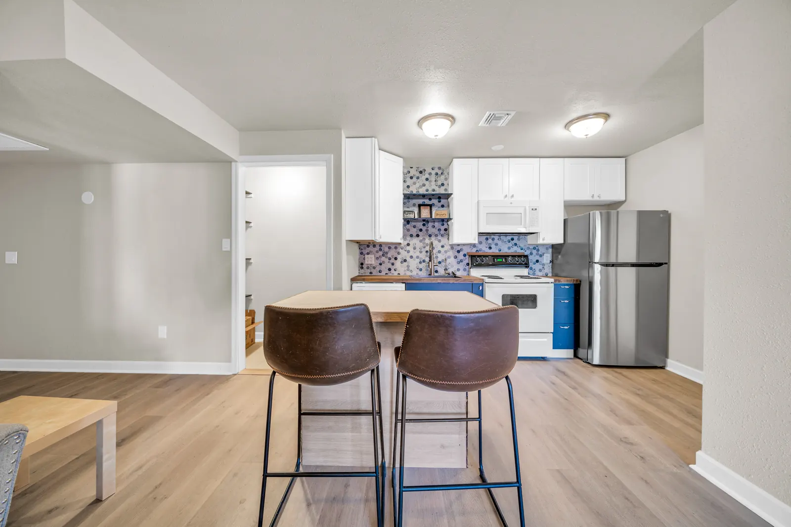 A kitchen with an island and two stools, white cabinets and a tiled backsplash.