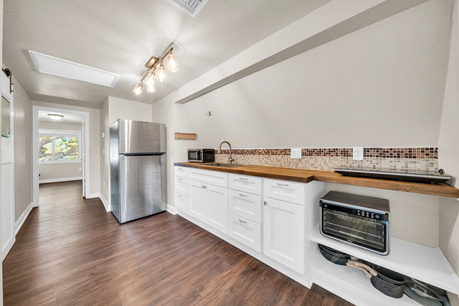 A galley kitchen with white cabinets, a butcher-block counter and a stainless refrigerator.