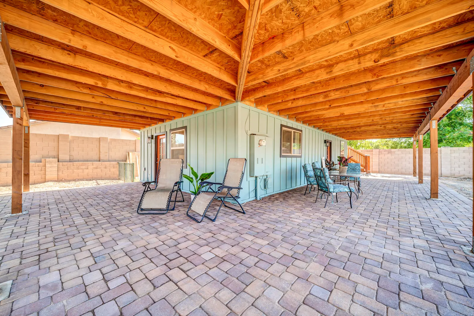 Reclining chairs and a houseplant on the paved patio, in the shade of the covered porch.